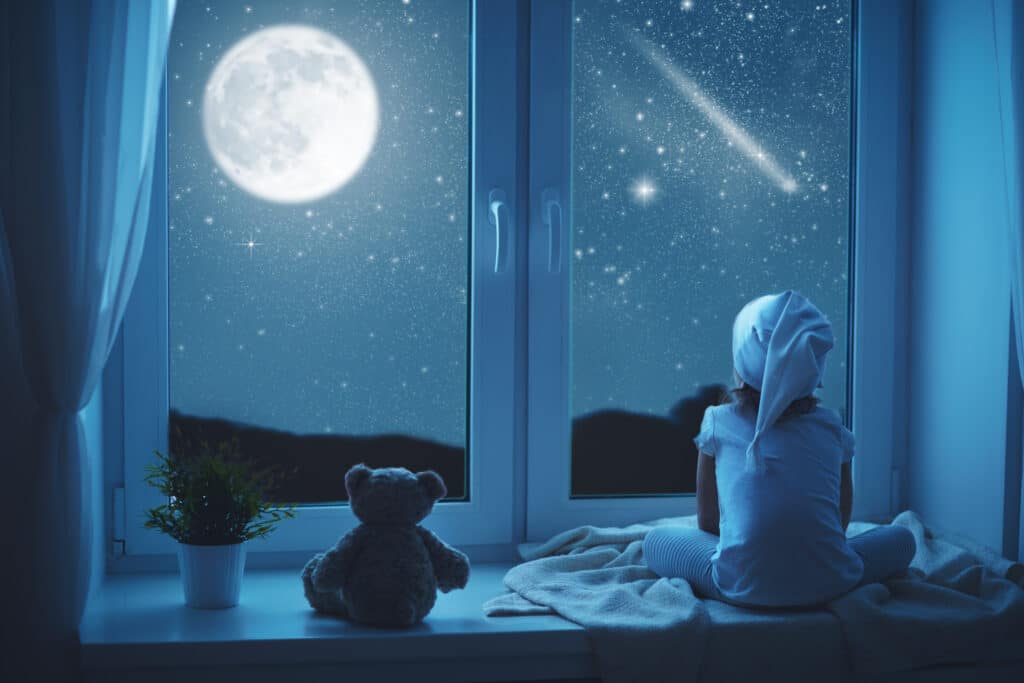 Ein Mädchen lauscht einer Gute-Nacht-Geschichte mit einem lieben Bär und schaut in die Sterne am Himmel